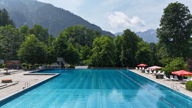 Schwimmbecken außen des Wellenberg Freibad. Im Hintergrund Bergkulisse und Bäume