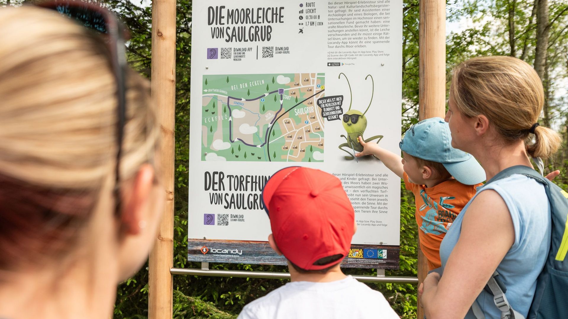 Personen stehen vor einem Schild mit Erklärungen beim Sinnenweg in Saulgrub