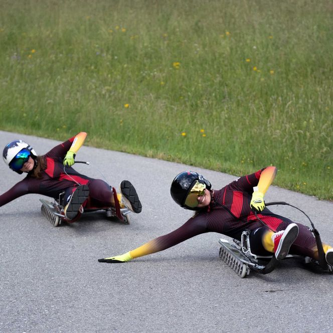 Zwei Rollenrodlerinnen in Rennanzügen fahren auf einer Straße durch eine Kurve.