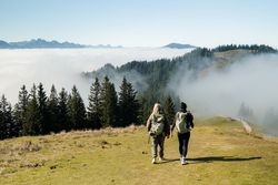 Zwei Frauen wandern auf einem Berg in der Sonne. Unten im Tal ist Nebel.