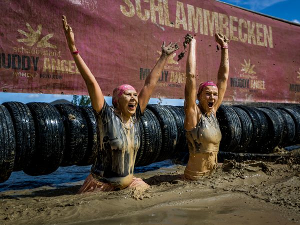 zwei Frauen im Schlammbecken, die die Arme zum Sieg in die Höhe strecken