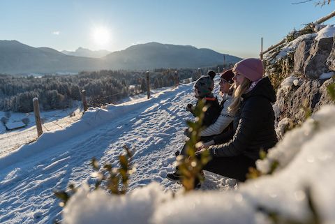 Eine Familie rastet nach der Winterwanderung in den Ammergauer Alpen auf einer Bank