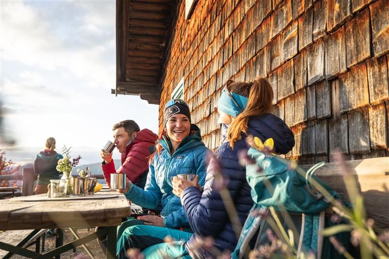 Zwei Frauen sitzen vor einer Hütte beim Wandern.