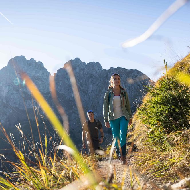 Zwei Wanderer marschieren auf einem schmalen Weg. Im Hintergrund sieht man die Klammspitze.