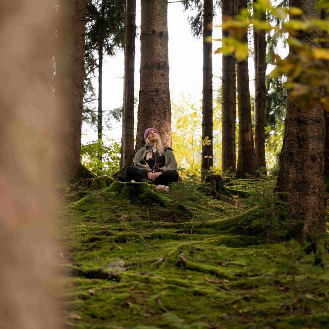 Eine Frau sitzt im Schneidersitz im Wald und genießt die Natur.