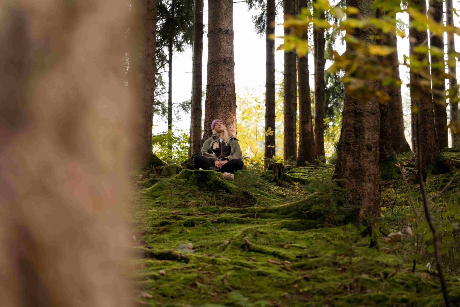 Eine Frau sitzt im Schneidersitz im Wald und genießt die Natur.