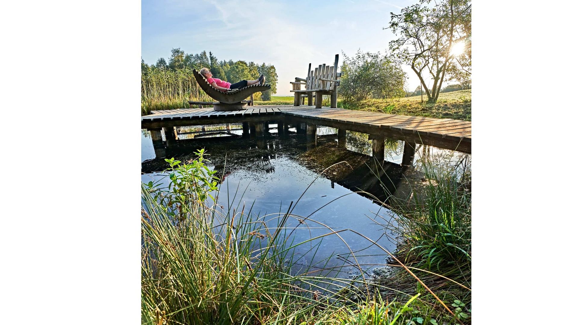 Eine Frau liegt auf einer Holzliege an einem kleinen Weiher
