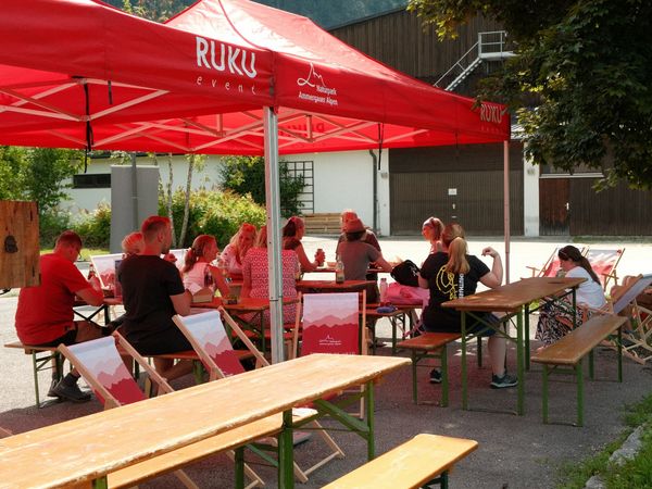 Die Teilnehmer sitzen beim Get-Together nach dem Müll sammeln unter roten Pavillionen zusammen.