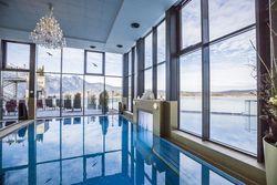 Innenbecken von Therme Trimini mit großen Fenstern, Kronleuchter und Blick auf den Kochelsee und die Berge.