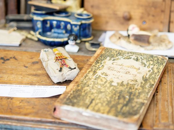 Ein alter Auftragsbuch liegt auf der Holzablage neben einer weiteren Holzspielfigur.